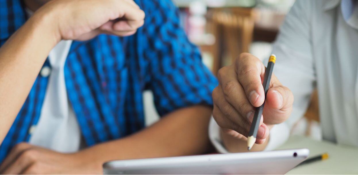 Two young people work over an electronic tablet