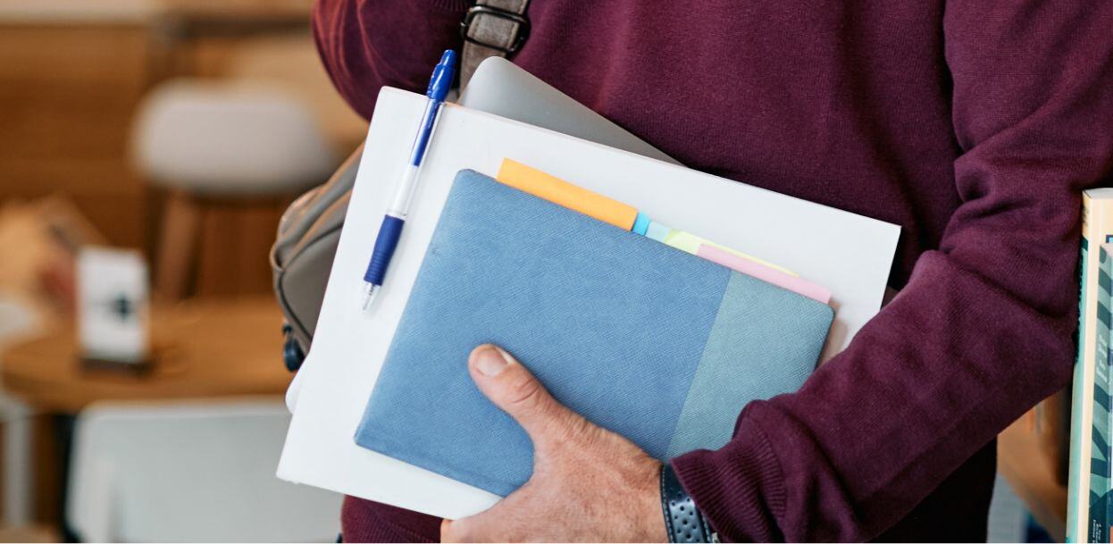 A close in photo of a student holding a stack of notes and an electronic tablet