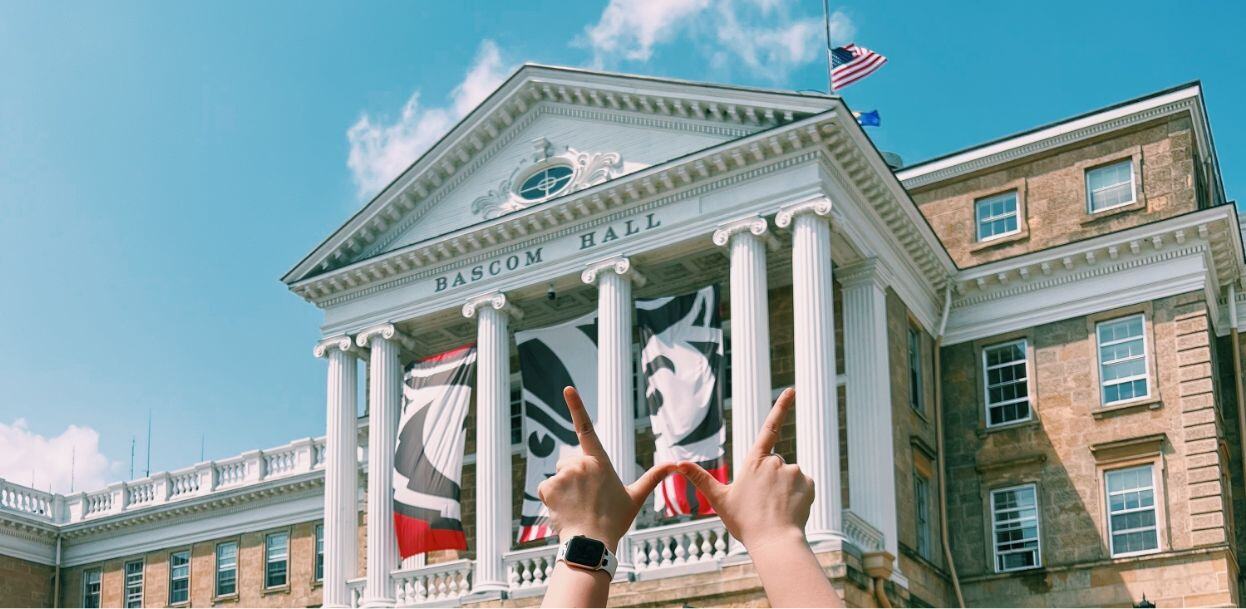 Two hands hold the shape of a W in front of the University of Wisconsin