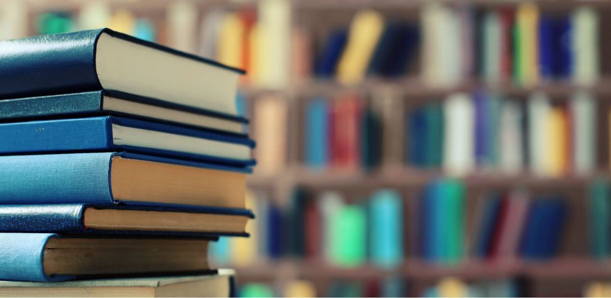 A stack of books in the foreground and rows a books on shelves in the background