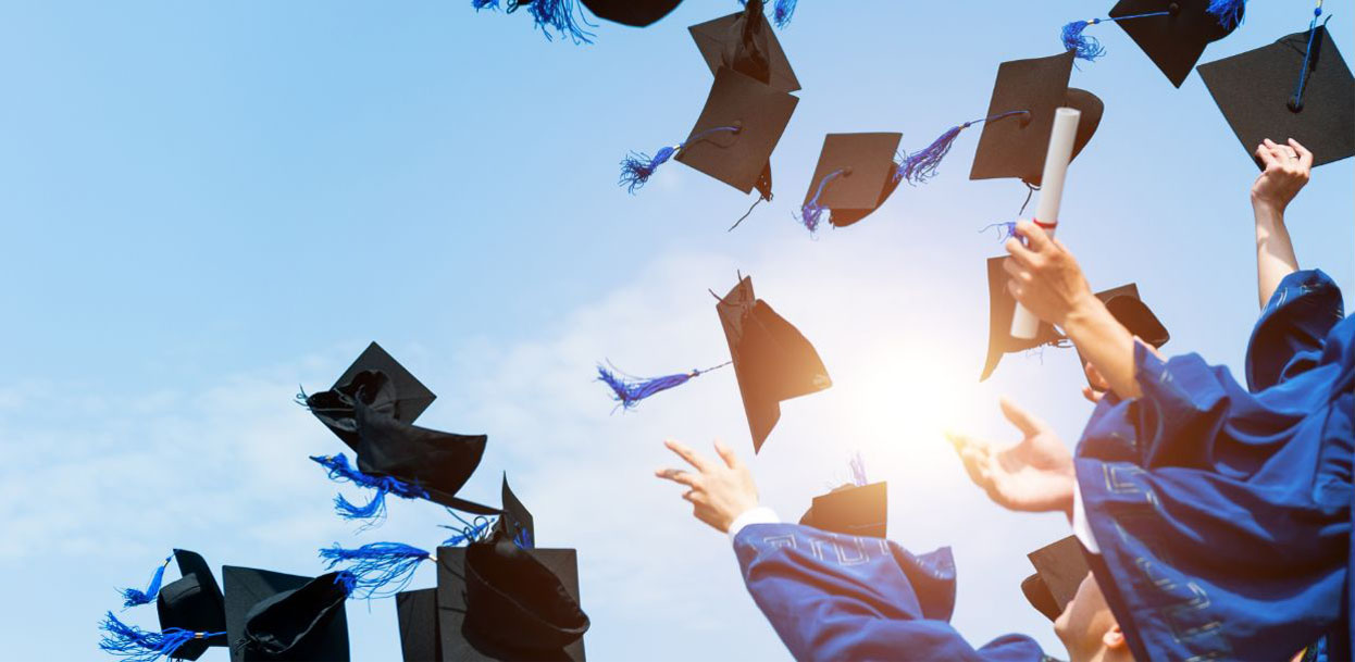 A group of graduates toss their caps into the blue sunny sky