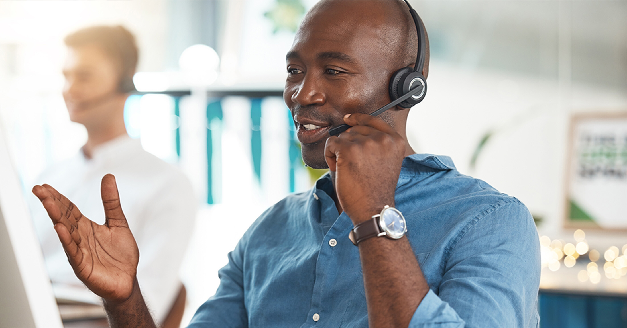 A smiling Attigo borrower services representative wearing a headset sits at a desk in front of a computer screen while assisting a student loan borrower over the phone.