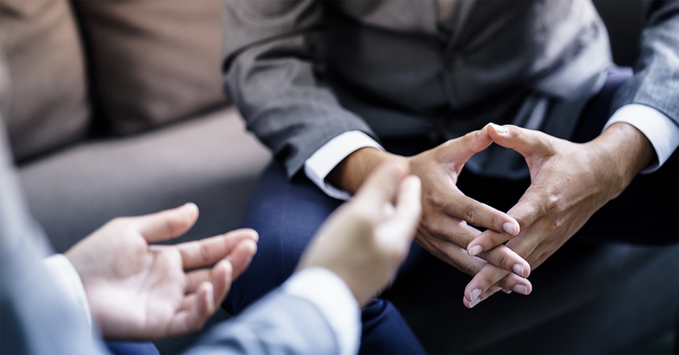 The hands of two coworkers sitting on a couch in an office discussing feedback.