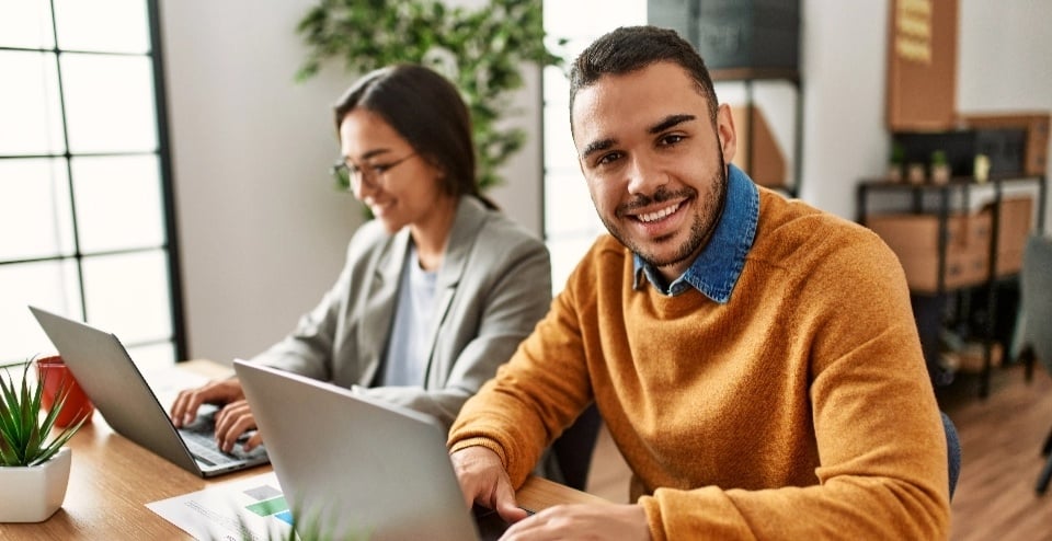 A man and woman smiling and working on laptops