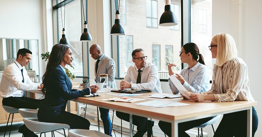 A group of employees in a collaborative training workshop gather around a table, actively engaged in a discussion related to skills development and training.